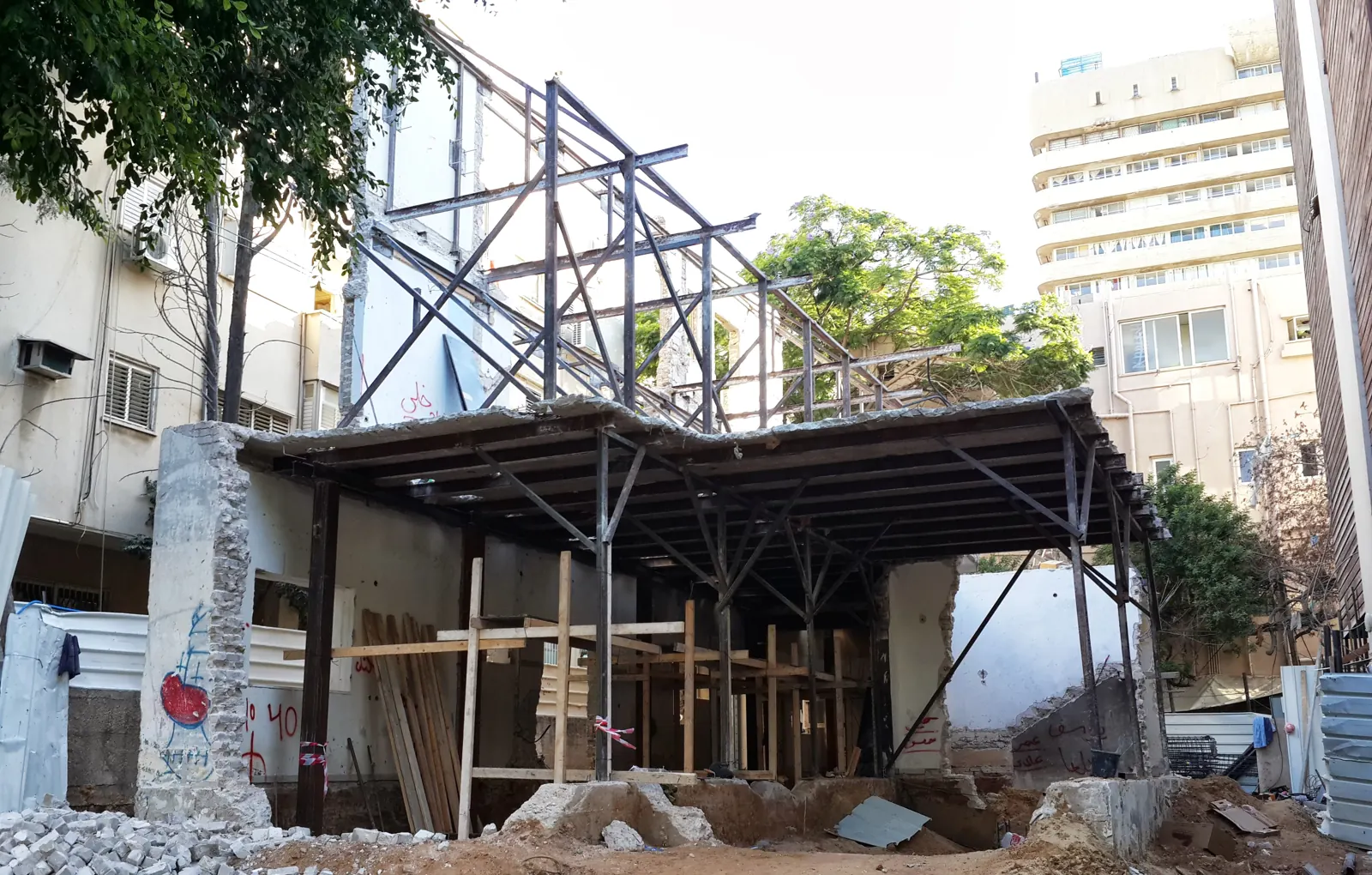 עמודי פלדה וחיזוקים אלכסוניים זמניים הנושאים תקרה וחזית של מבנה לשימור מעל חפירת מרתף בתל אביב